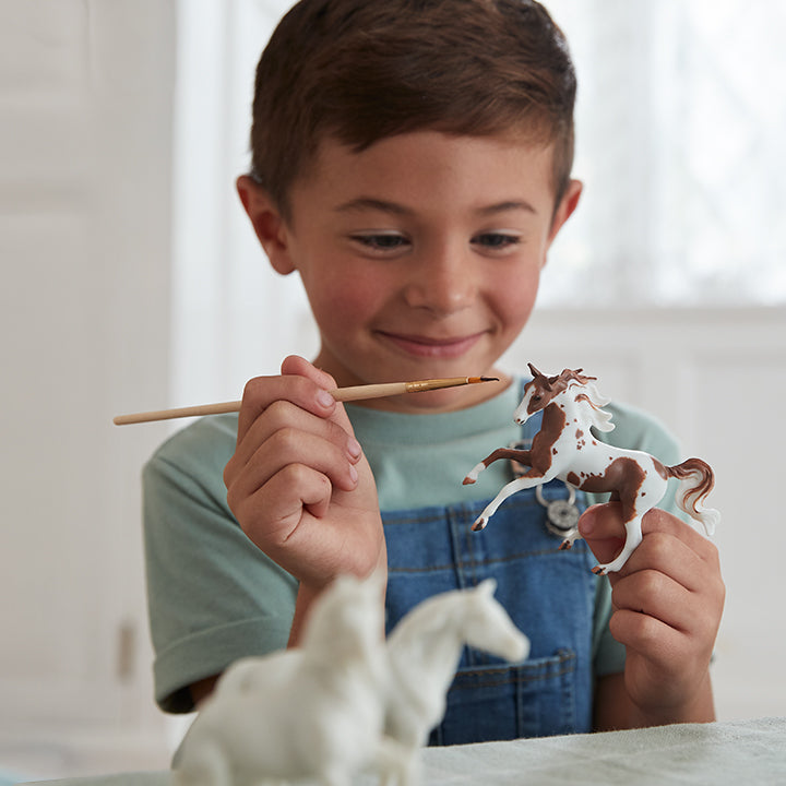 A child painting a Breyer Stablemates model inside a house