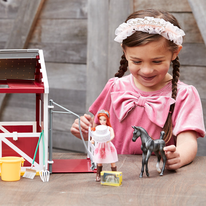 A child playing with the Birthday at the Barn playset in front of a barn door.