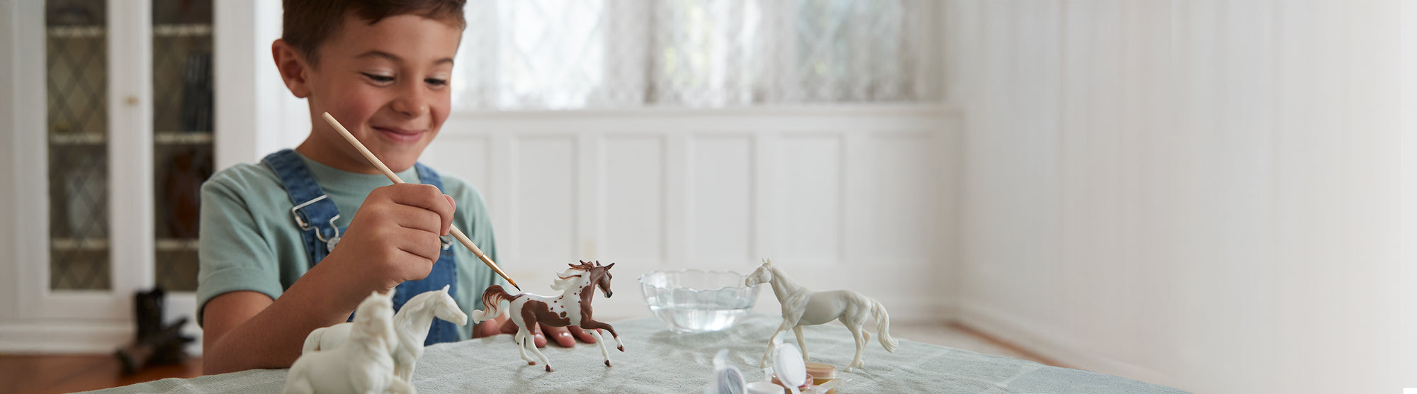 A child painting a Breyer model from a craft set with a paint brush and a bowl of water.