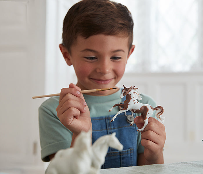 A child painting a Breyer model from a craft set.