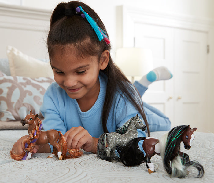 A child on a bed playing with Breyer's Mane Beauty toys