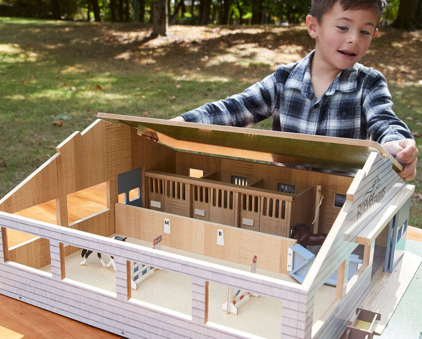 A boy playing with the Deluxe Arena Stable outside on a table