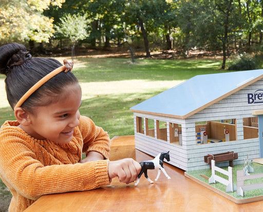 A girl playing with the Deluxe Arena Stable outside on a table