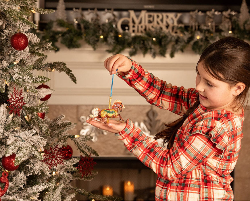 A child holding the Fleur | Carousel Ornament next to a Christmas tree.