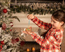 A child holding the Fleur | Carousel Ornament next to a Christmas tree.