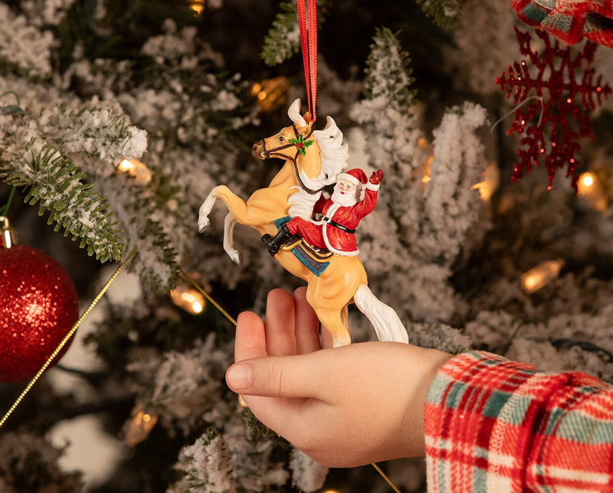 A child's hand holding the Hi Ho Santa | Santa Ornament on a Christmas tree