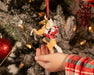 A child's hand holding the Hi Ho Santa | Santa Ornament on a Christmas tree