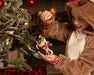 A child's in bear pajamas  holding the Hi Ho Santa | Santa Ornament near a Christmas tree