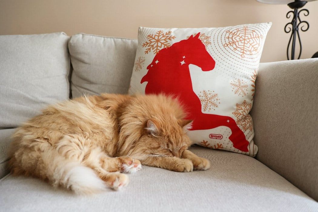 Red horse pillow on sofa with orange cat