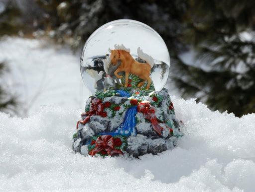 Breyer holiday snow globe with two horses in a winter scene on a rock-like base featuring a stream and adorned with ribbons and berries